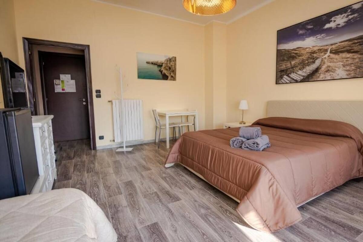 Una habitación de hotel con cama, escritorio, silla, radiador y un cuadro en la pared.