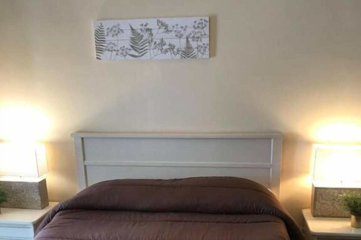 Un dormitorio con cama, cabecera, mesitas de noche y decoración en la pared.