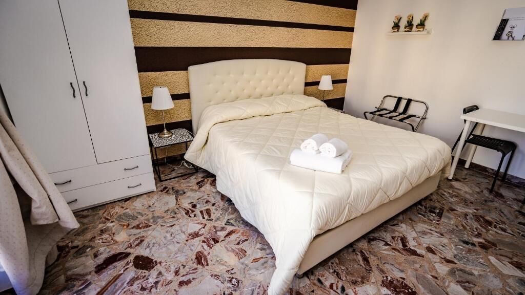 Quarto de hotel com uma cama grande, um guarda-roupa, uma escrivaninha e uma cadeira.