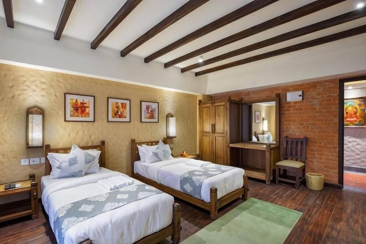 A room with two beds, wooden beams, a brick wall, and a green rug.