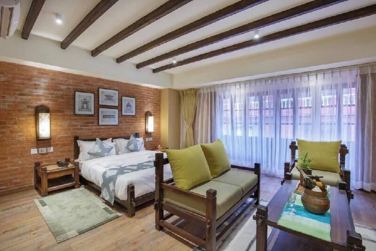 A room with a bed, a sofa, a wooden table with a plant, and a window with curtains.