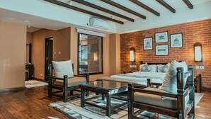 A modern hotel room with a large bed, a seating area with a glass table, and a brick wall with framed pictures. - Hotel Thamel House (Kathmandu)