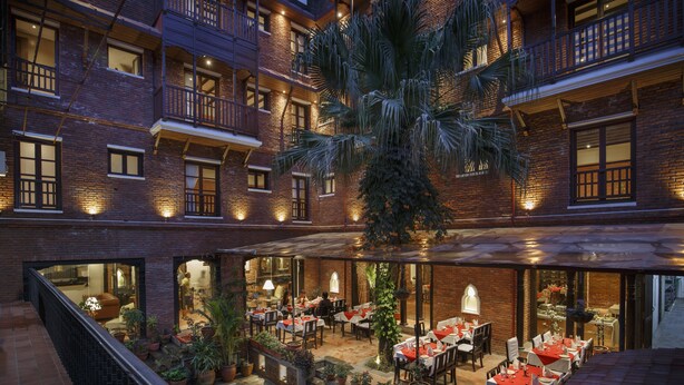 A multi-level outdoor dining area with brick walls, potted plants, and tables set for dining. - Hotel Thamel House (Kathmandu)