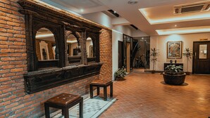 A hallway with a brick wall, a wooden bench, a large mirror, and a potted plant. - Hotel Thamel House (Kathmandu)
