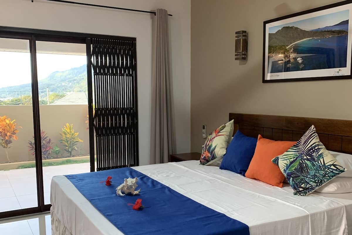 A hotel room with a large bed, a ceiling fan, a view of the outdoors, and a framed picture on the wall.