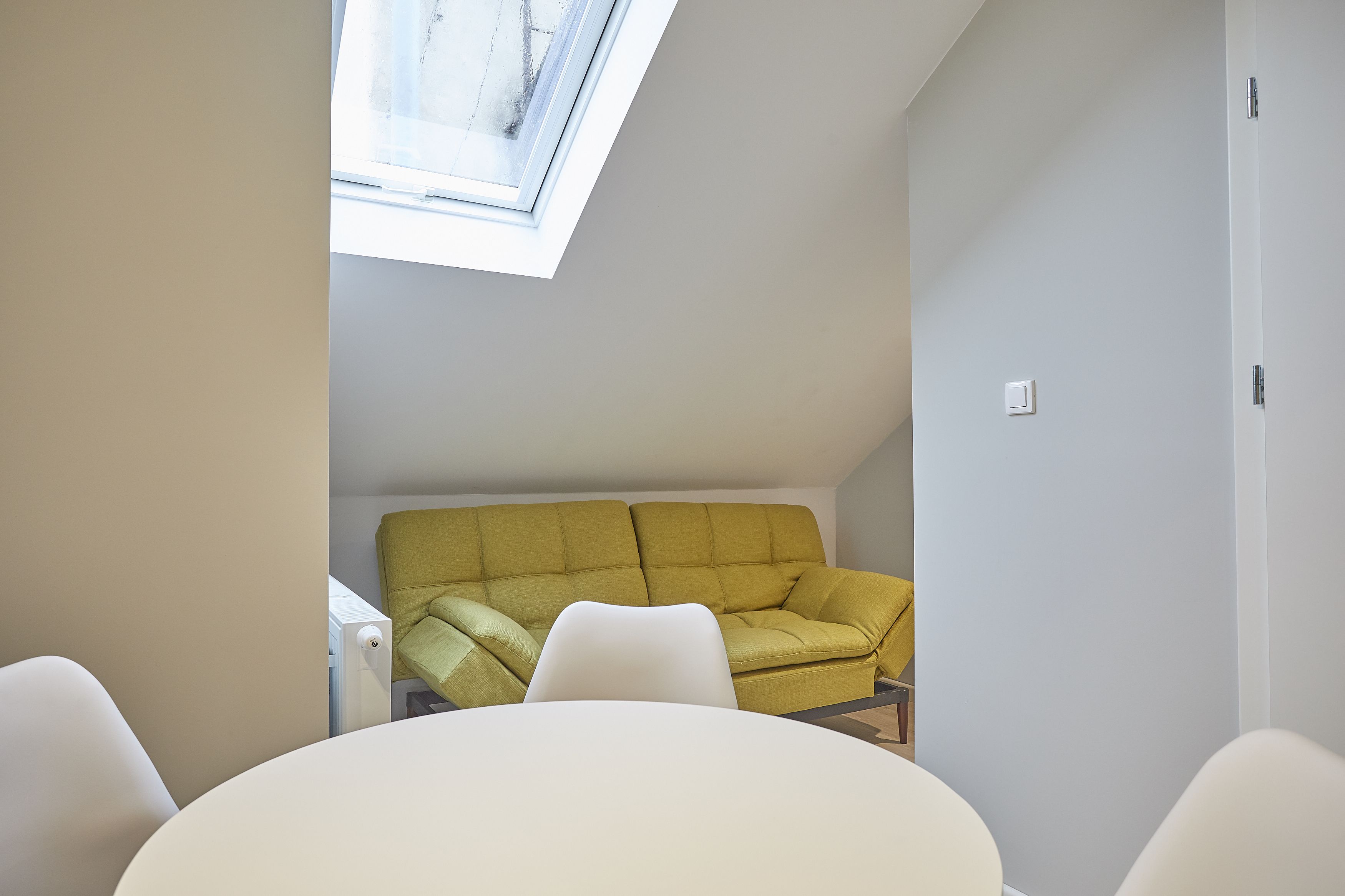 A modern room with a yellow sofa, white chairs, and a skylight.