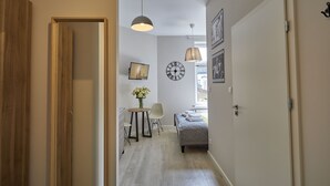Un couloir avec un lit, une petite table sur laquelle est posé un vase de fleurs et une horloge au mur.