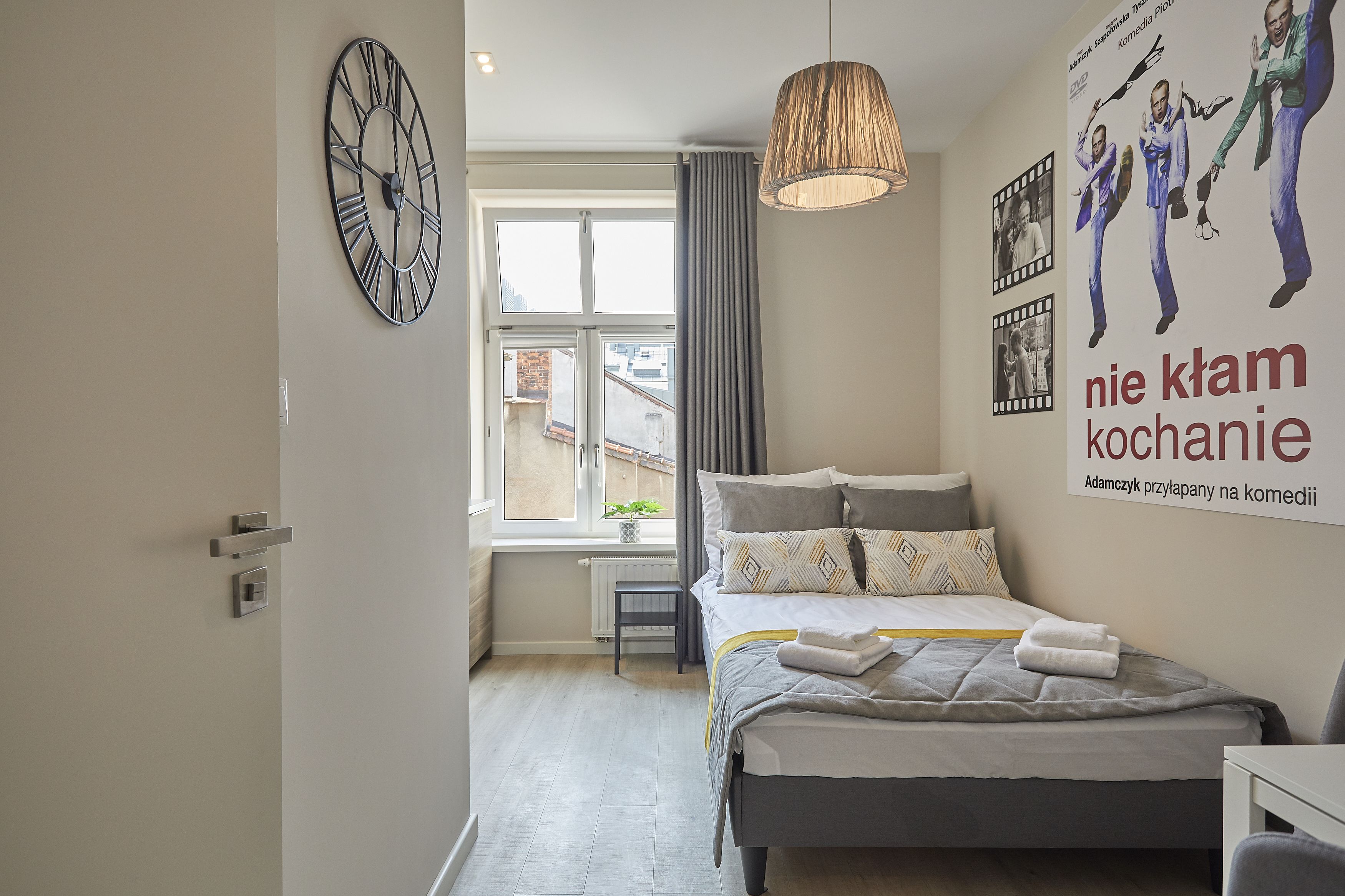 A modern bedroom with a bed, a large wall clock, a poster, and a window with curtains.