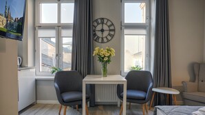 Une pièce moderne avec une table blanche, deux chaises grises, une horloge et un vase rempli de fleurs.