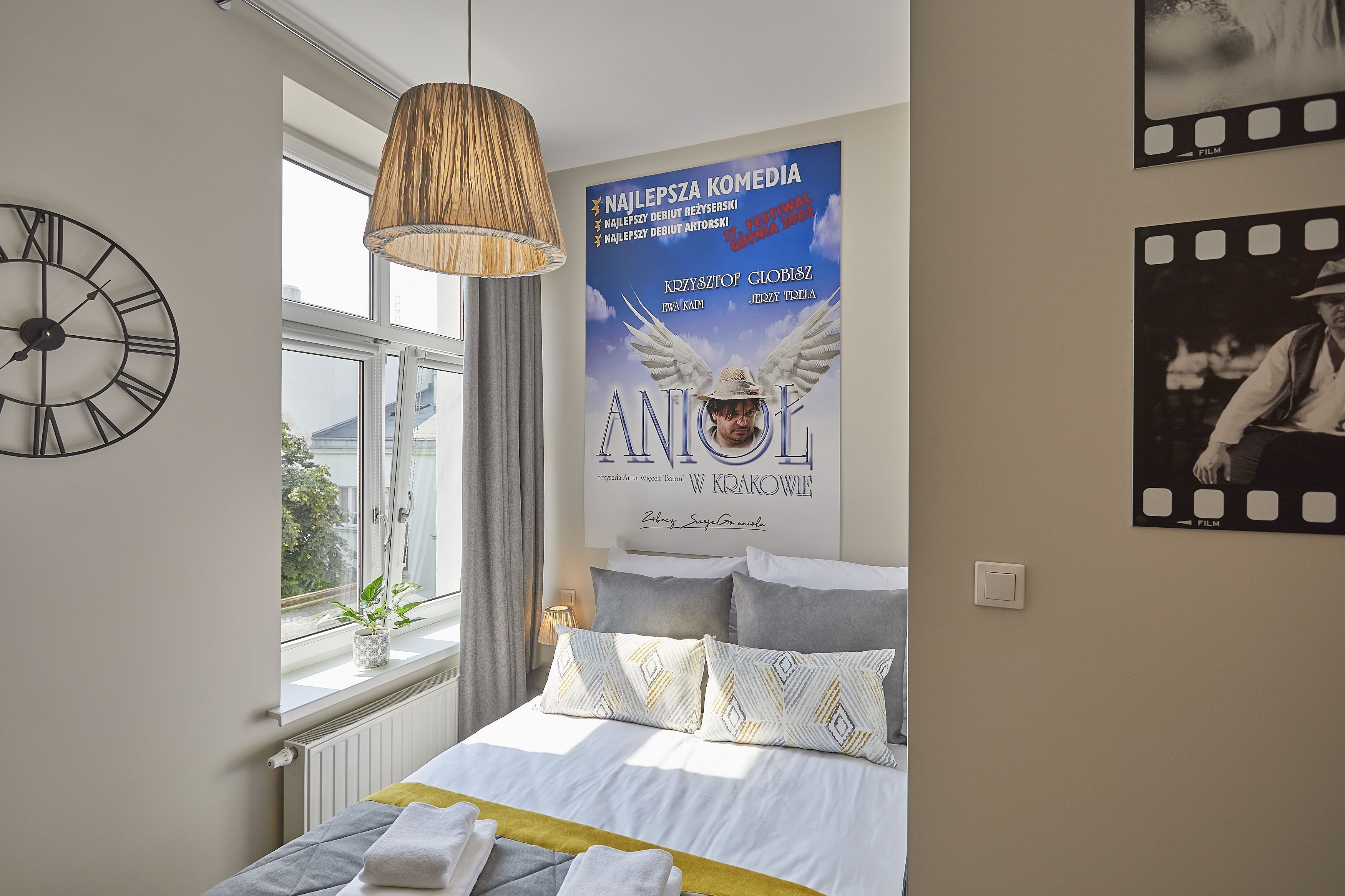 A bedroom with a large bed, a wall clock, a poster, and a window with a view.