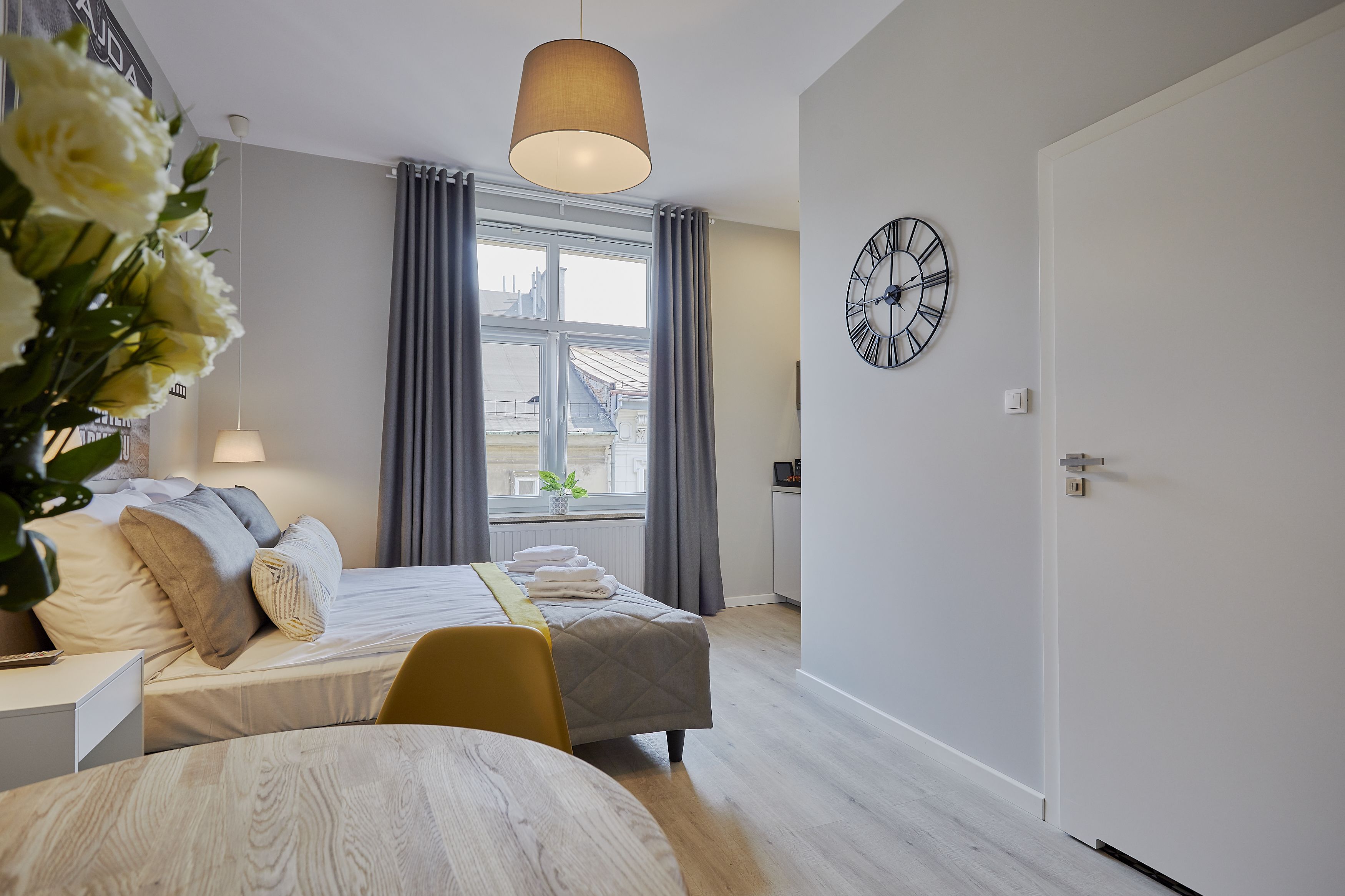 Een moderne slaapkamer met een bed, nachtkastje, lamp en een groot raam met gordijnen.