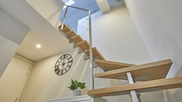 Un escalier moderne avec des marches en bois et des rampes en métal, une horloge murale et une plante en pot.