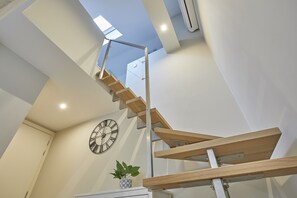 A modern staircase with wooden steps and metal railings, a wall clock, and a potted plant. - Florianska 32 by PI Apartments (Kraków)