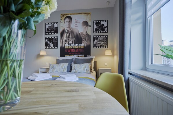 Une chambre d’hôtel avec un lit, des lampes de chevet, une affiche au mur et une fenêtre donnant sur un paysage.