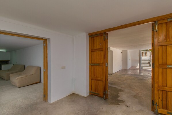 Una habitación con un sofá color beige, puertas de madera y una escalera al fondo.