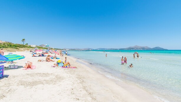 A beach with clear turquoise water, people sunbathing, and umbrellas. - Villa Canta House only 60 meter to the beach (Playa de Muro)