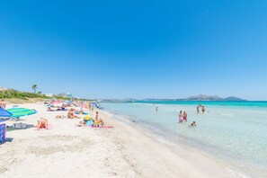 Una playa con agua turquesa cristalina, gente tomando el sol y sombrillas.