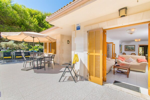 An outdoor seating area with tables and chairs, a sofa inside, and a door leading to the interior.