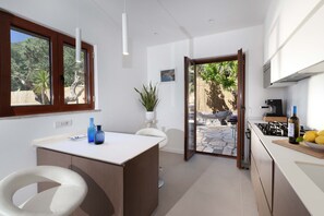 A modern kitchen with a central island, white bar stools, and a view of the outdoor area.