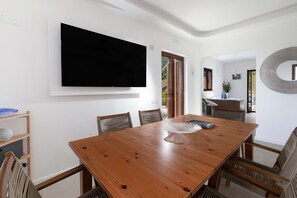 A dining area with a wooden table, chairs, a television mounted on the wall, and a view of the outdoors. - AMORE RENTALS - Villa Marina with Private Pool, Sea View, Terraces and Parking (Massa Lubrense)
