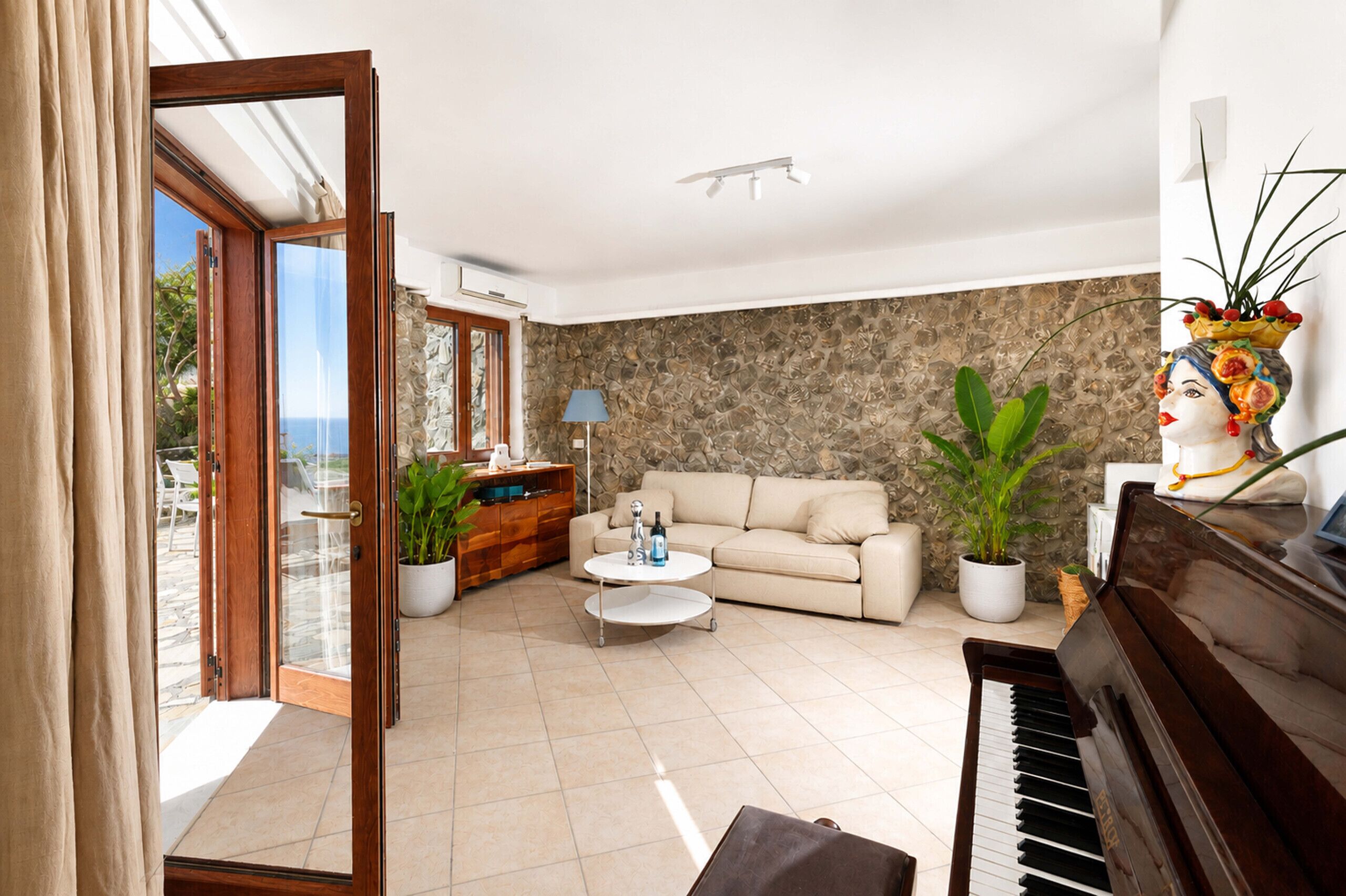 Un salón con un sofá color crema, una mesa de centro, un piano y una pared de piedra.