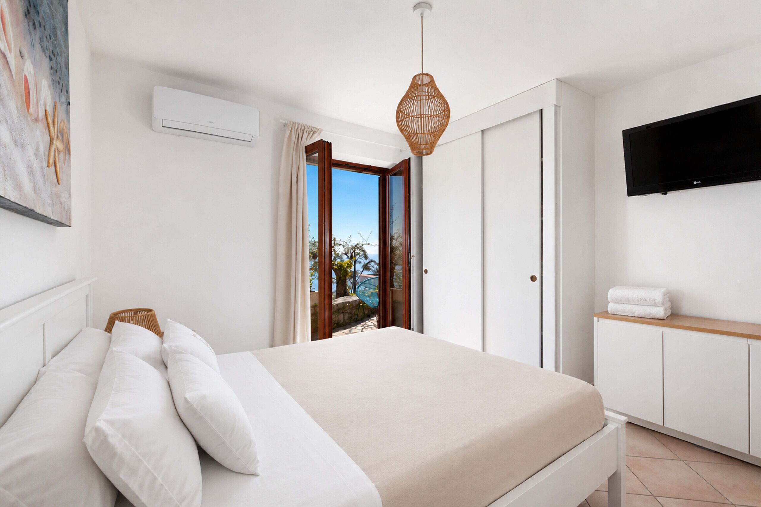 Un dormitorio con cama, televisor montado en la pared y vista al exterior.