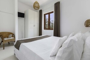 Una camera da letto con un letto grande, una sedia in vimini, un armadio e una finestra con tende.