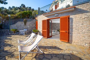 A stone building with a balcony, a stone patio with lounge chairs, and a table with chairs.