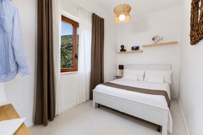 A bedroom with a bed, a window with curtains, a bedside table, and wall-mounted shelves with decorative items.
