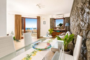 Un soggiorno moderno con un tavolo in vetro, divani bianchi, una parete d'accento in pietra e vista sul mare.