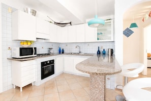 A modern kitchen with white cabinets, a microwave, stove, oven, and a granite countertop island. - AMORE RENTALS - Villa Marina with Private Pool, Sea View, Terraces and Parking (Massa Lubrense)