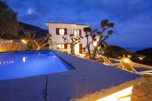 Una piscina con bordo in pietra, un edificio bianco con molte finestre e alcuni alberi.