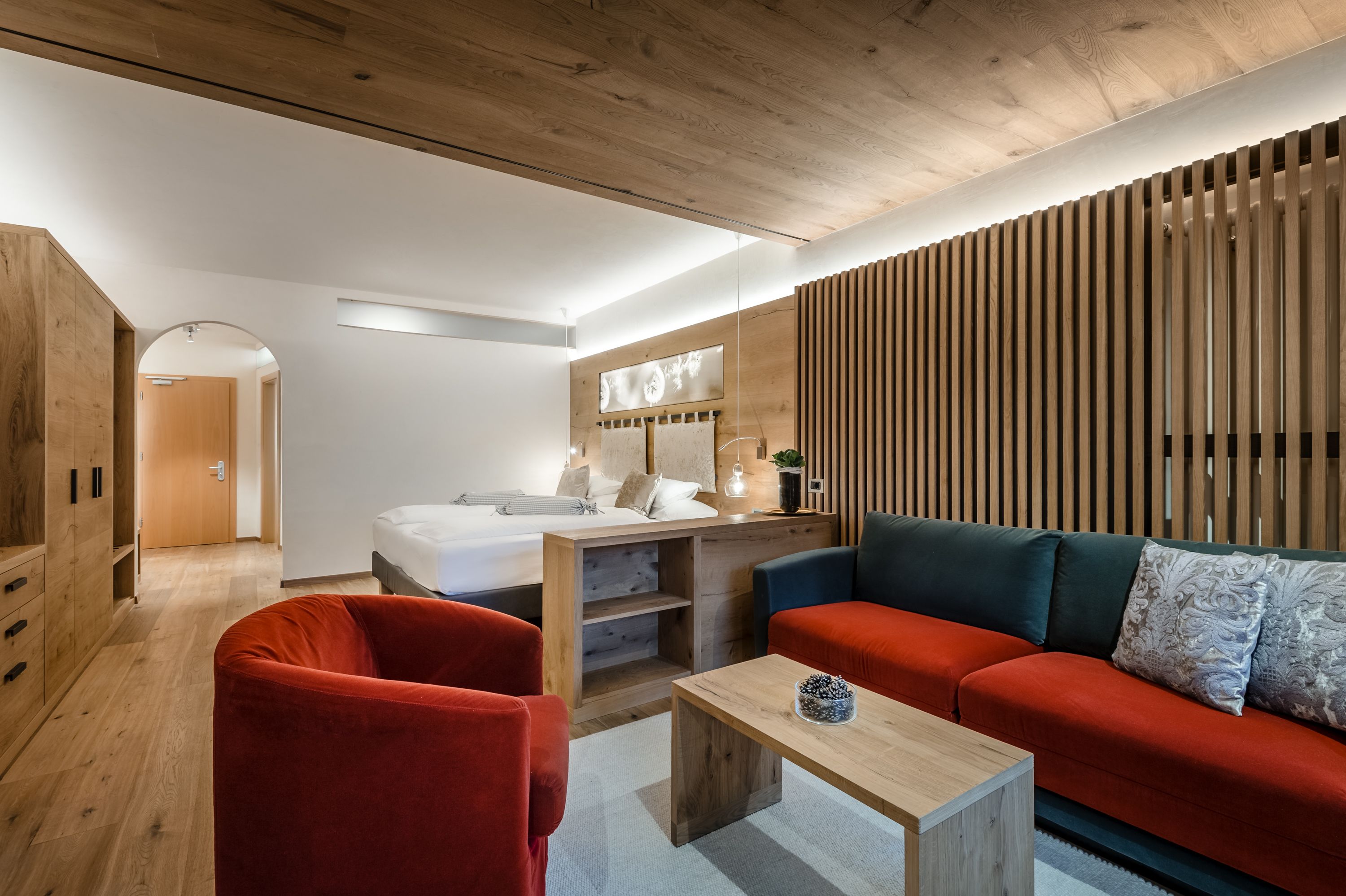 A modern room with a wooden ceiling, a red sofa, a wooden table, and a bed with a wooden headboard.