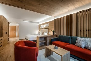 A modern room with a wooden ceiling, a red sofa, a wooden table, and a bed with a wooden headboard. - Hotel La Majun (Badia)