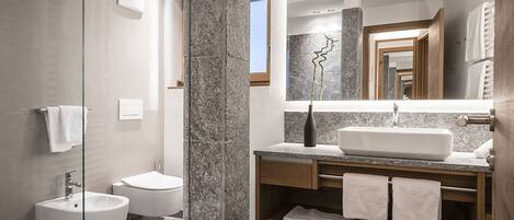 Une salle de bain moderne dotée d’une douche à parois de verre, d’un bidet sur pied, d’un grand miroir et d’un meuble-lavabo avec un évier et un porte-serviettes.