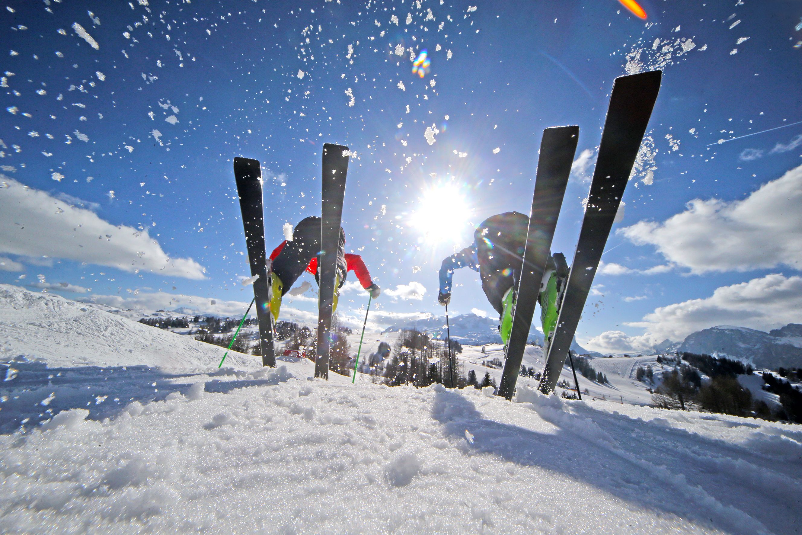 Pendenza innevata per sci con bastoncini da sci e un sole luminoso sullo sfondo.