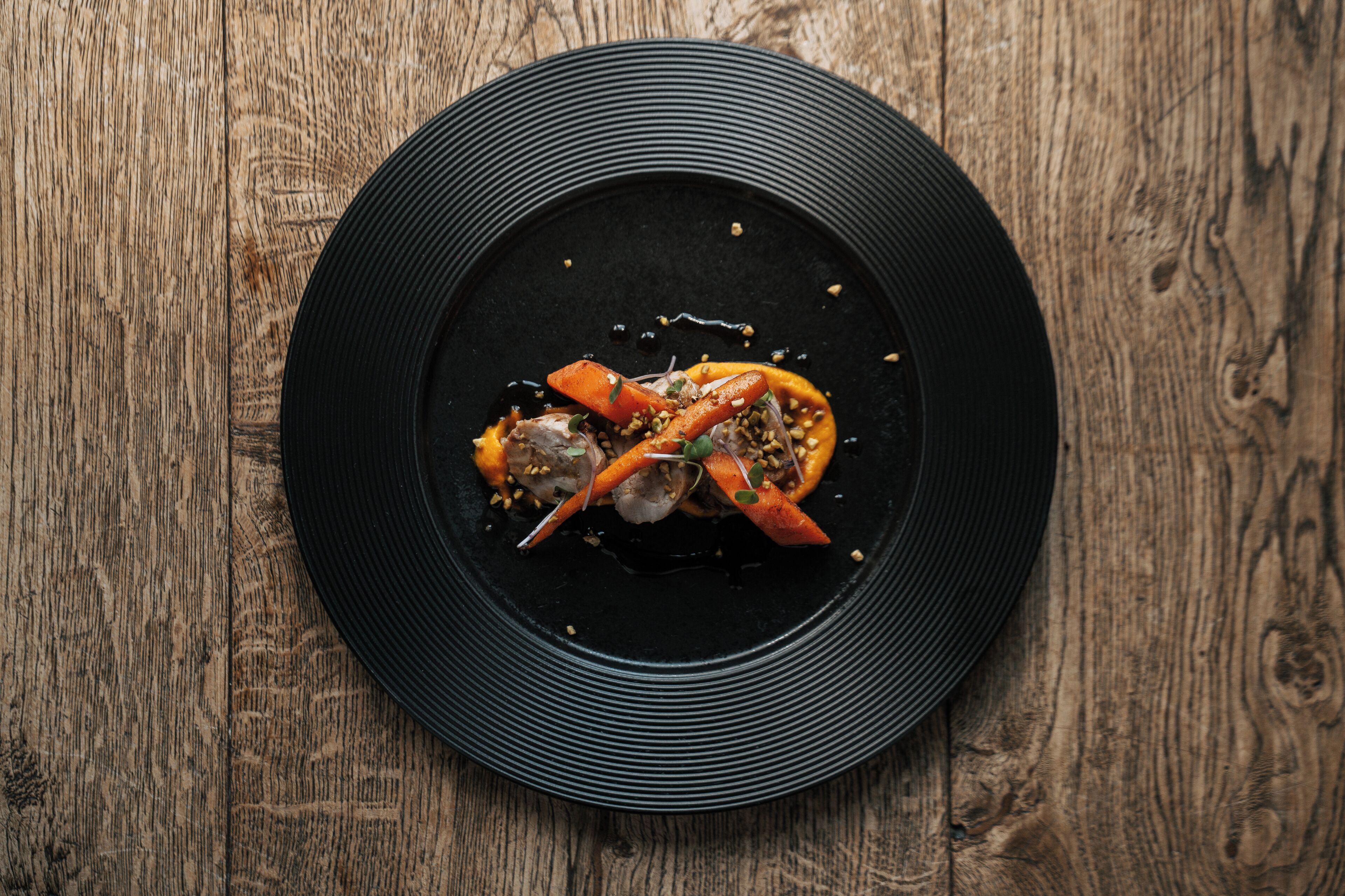 A black plate with a seafood dish on a wooden table.