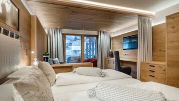 A hotel room with two beds, a desk, a TV, and a view of the outside.
