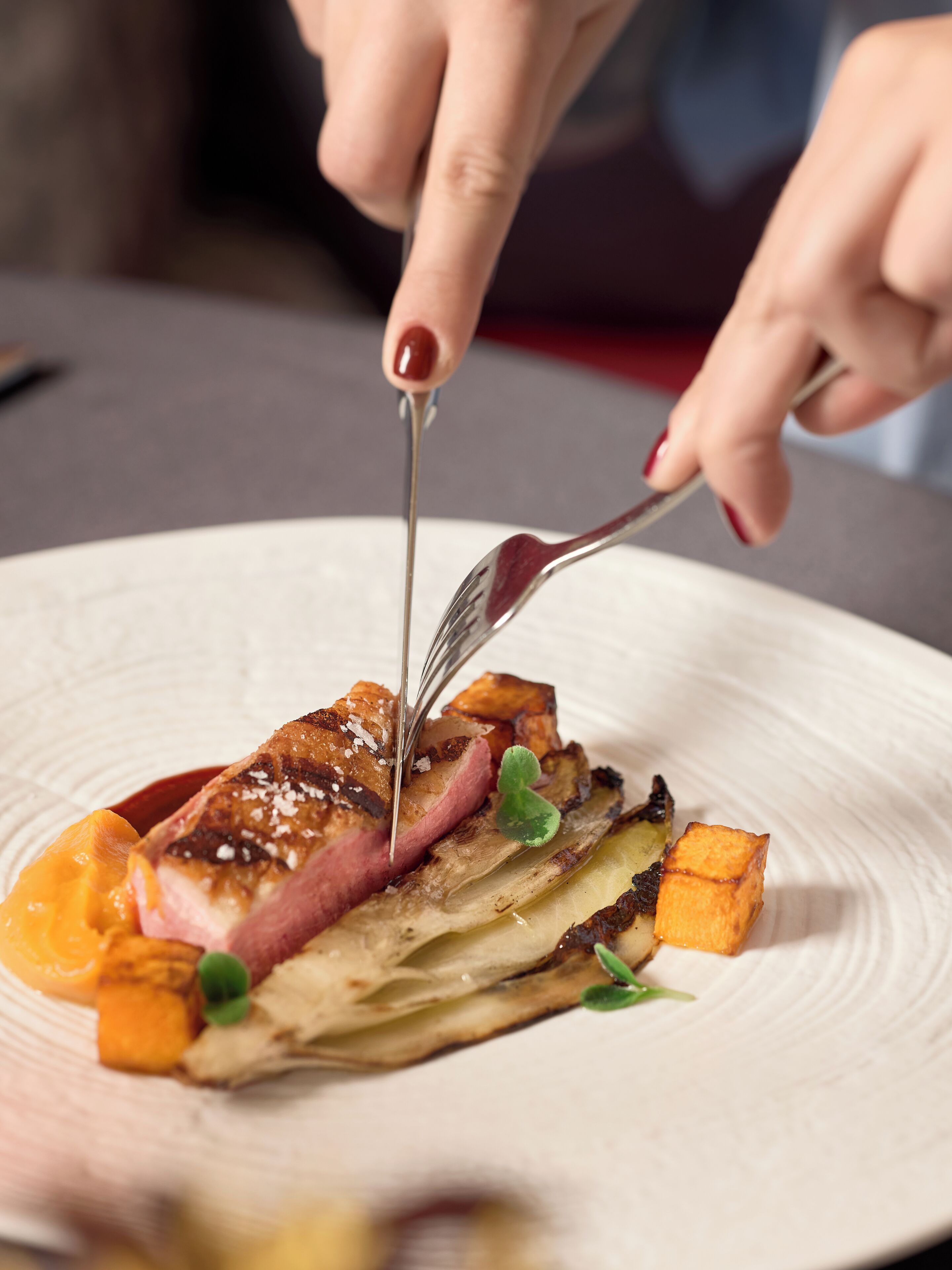 A person cutting a dish with a fork and knife.
