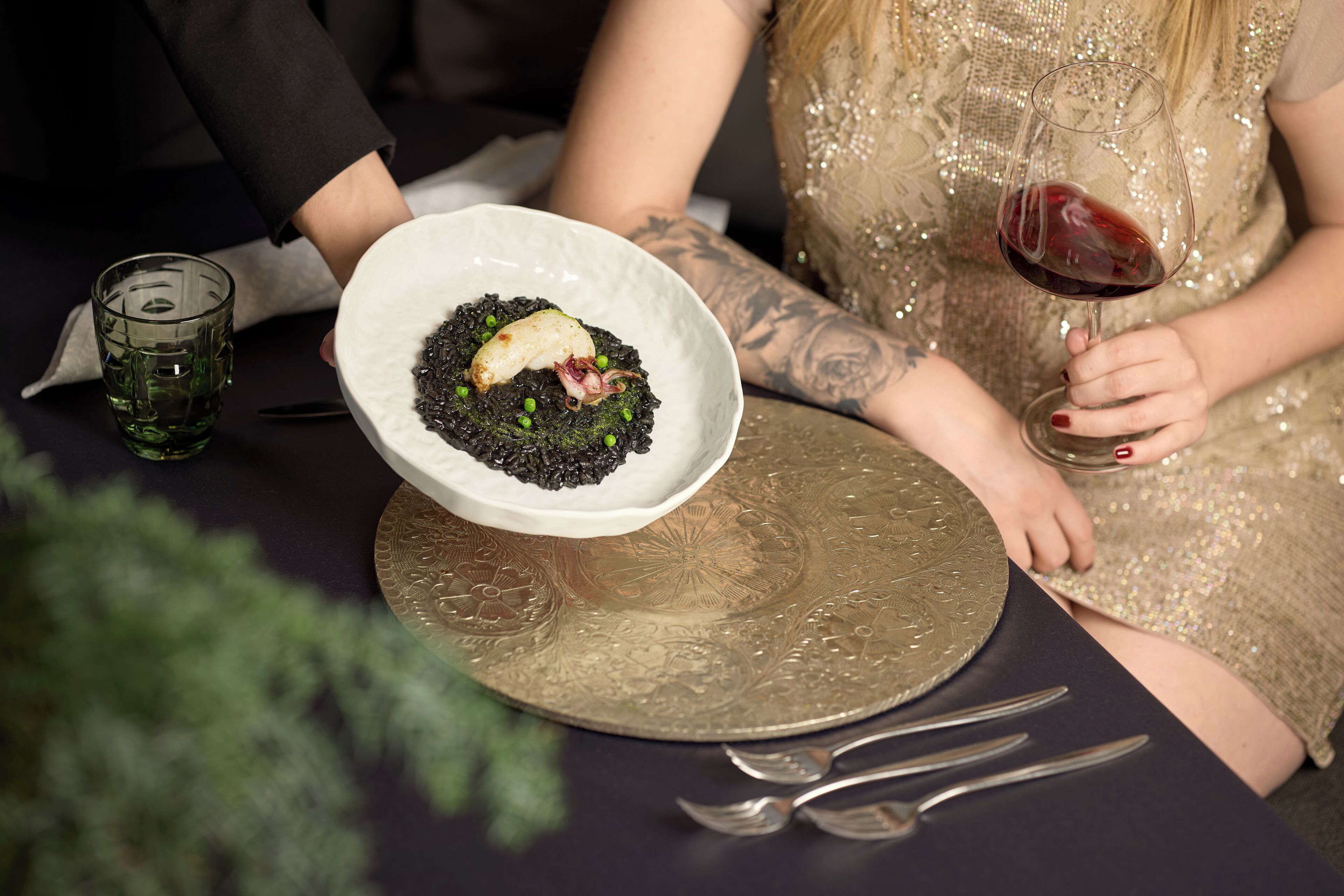 A dining table with a plate of food, a glass of red wine, and a decorative plate.
