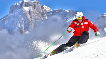 Ein Skifahrer in einer roten Jacke fährt einen verschneiten Hang hinab, im Hintergrund ist ein felsiges Gebirge zu sehen.