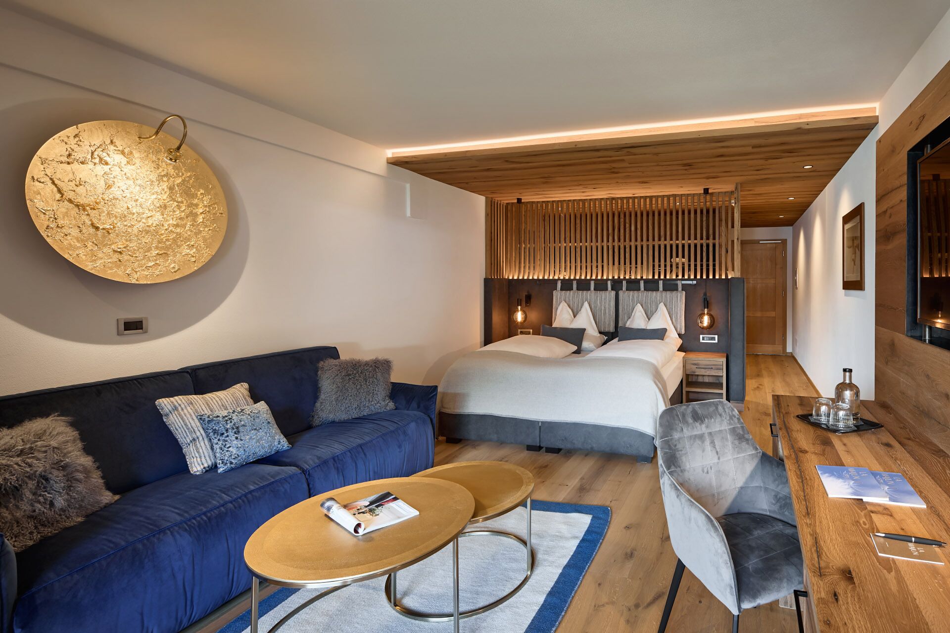 Une chambre d’hôtel moderne avec un grand lit, un canapé bleu, une table basse en bois et un bureau avec une chaise.