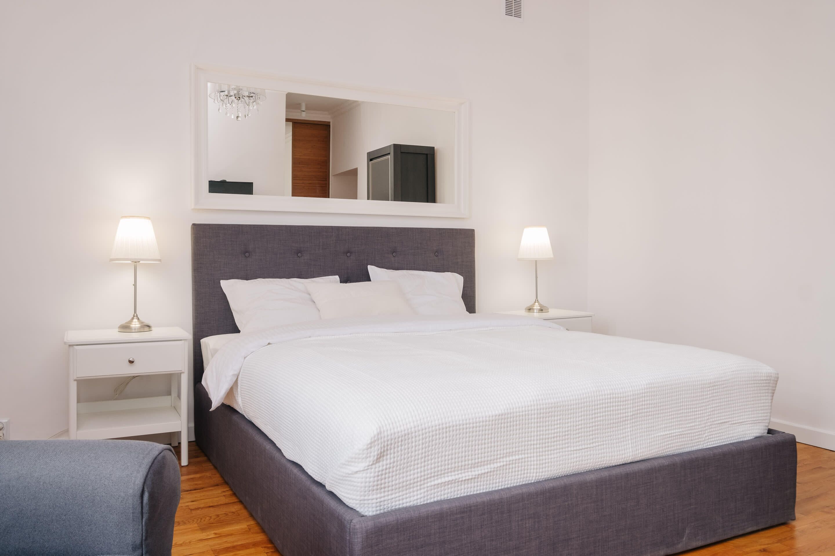 A neatly arranged bedroom with a large bed, two bedside tables, a mirror, and a chandelier.
