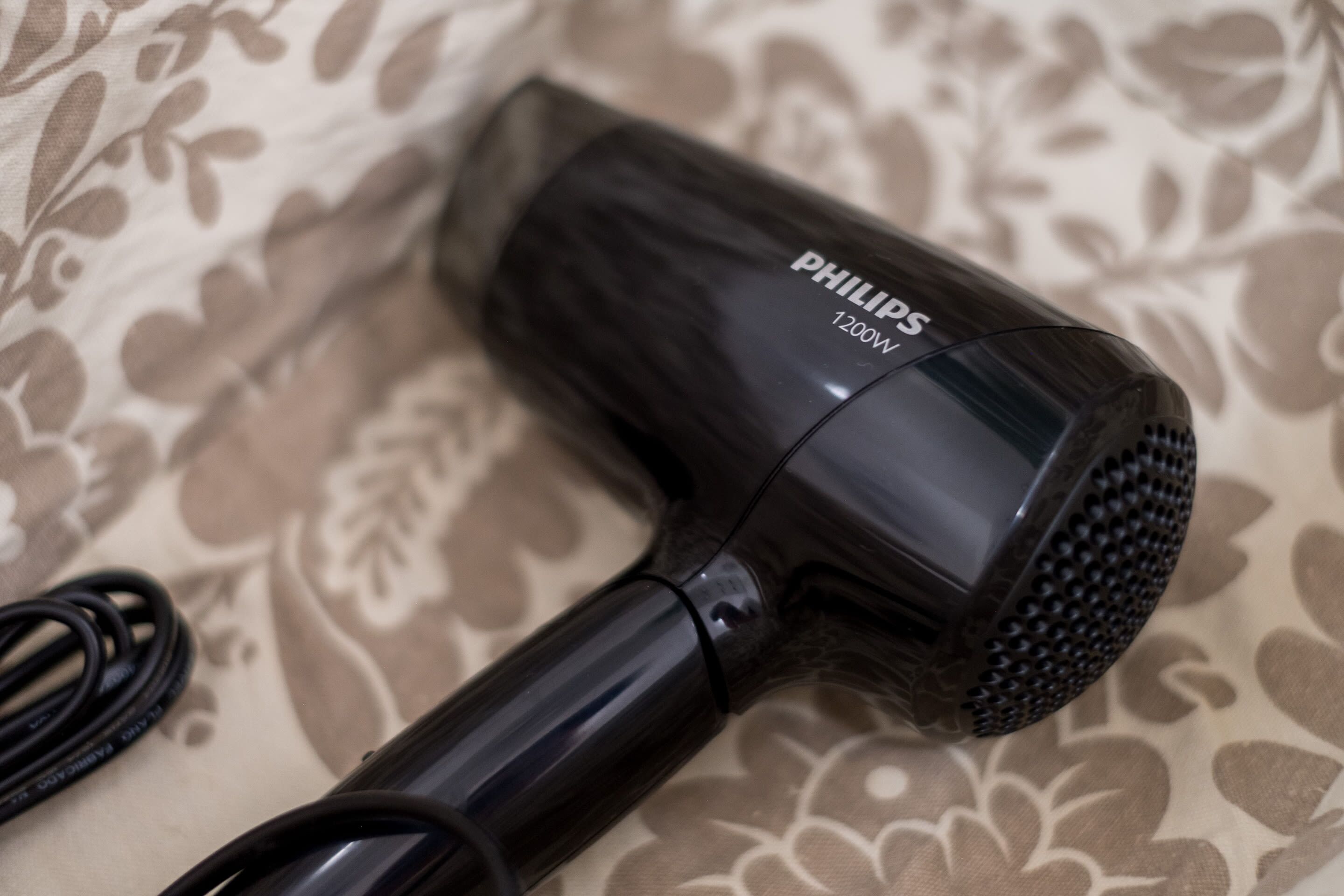 A Philips 1200W hair dryer on a patterned fabric surface.