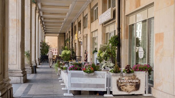 A corridor with columns, a cafe area with outdoor seating, and a sign for 'WESZ COZHSZ'. - Plac Konstytucji Studio (Warsaw)
