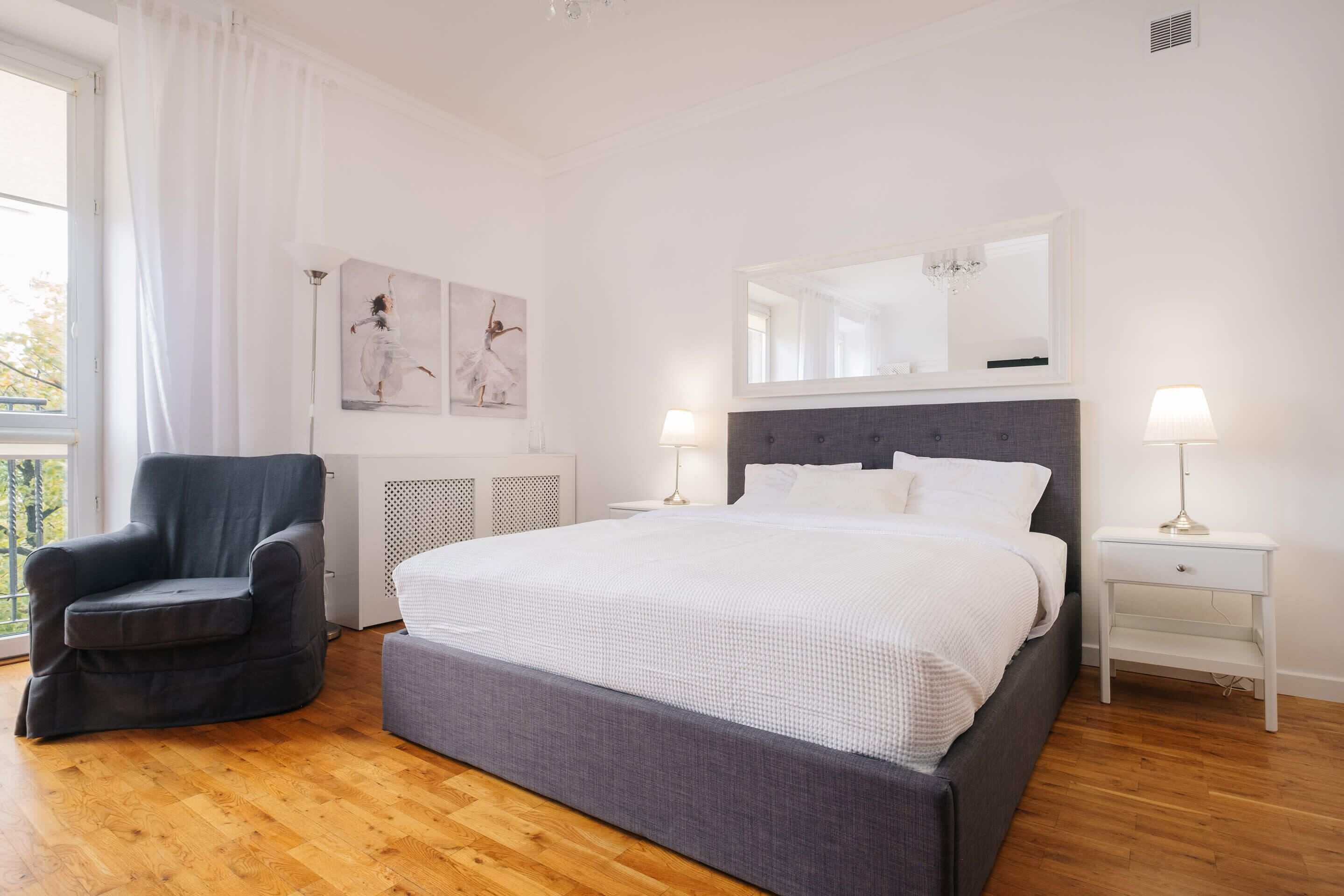 A bedroom with a large bed, a chair, a nightstand, and a window with curtains.