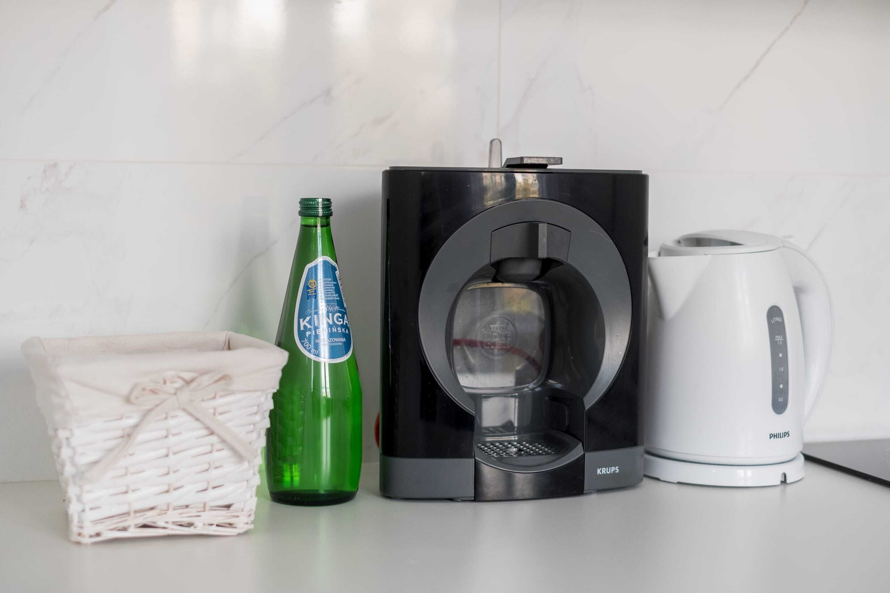 A kitchen with a coffee maker, a kettle, and a bottle of beer.
