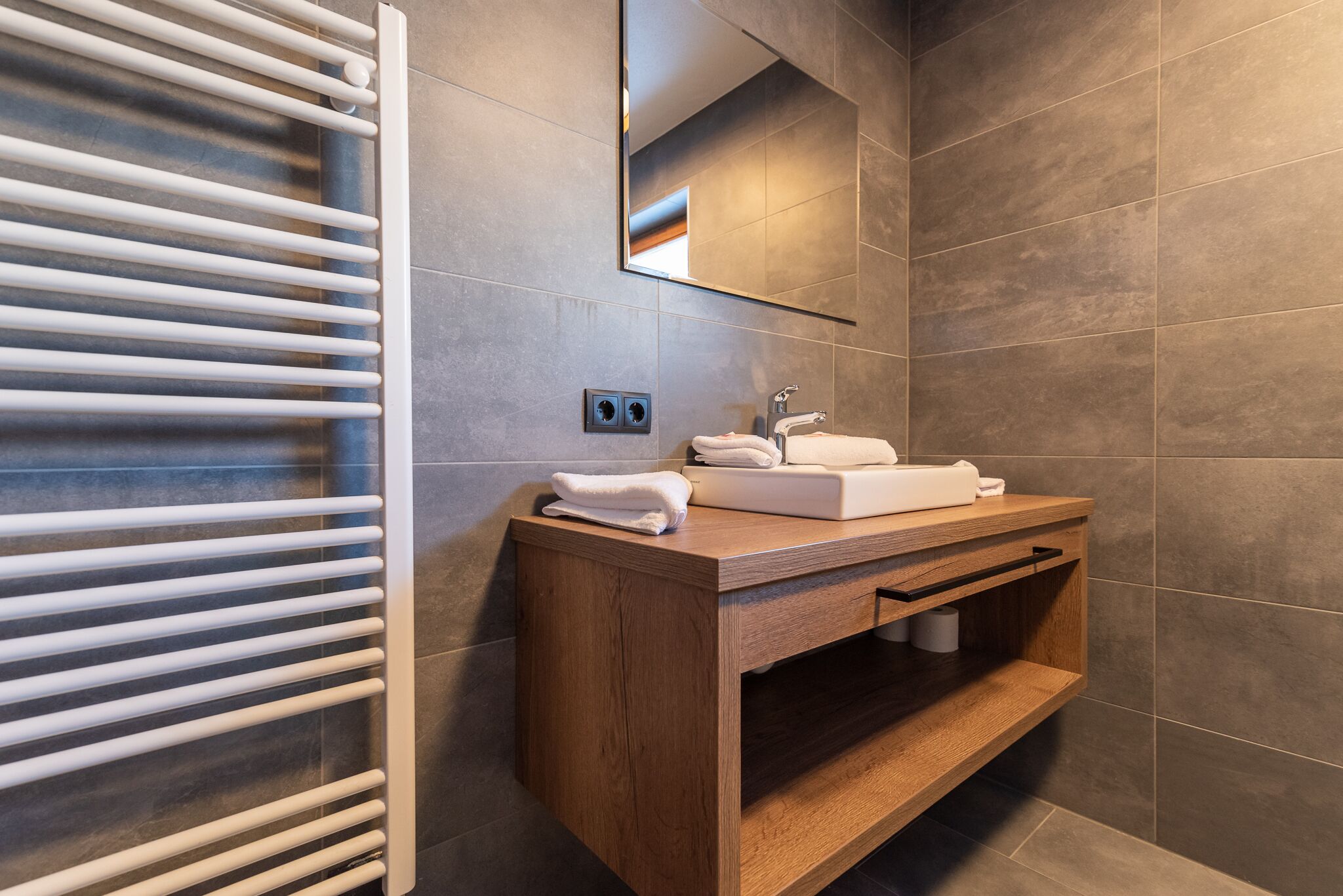 A modern bathroom with a wooden vanity, a white sink, and a towel rack.