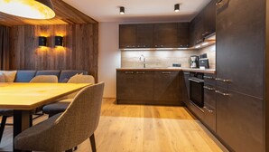 Uma cozinha moderna com armários escuros, uma mesa de jantar de madeira e duas luzes fixadas na parede.