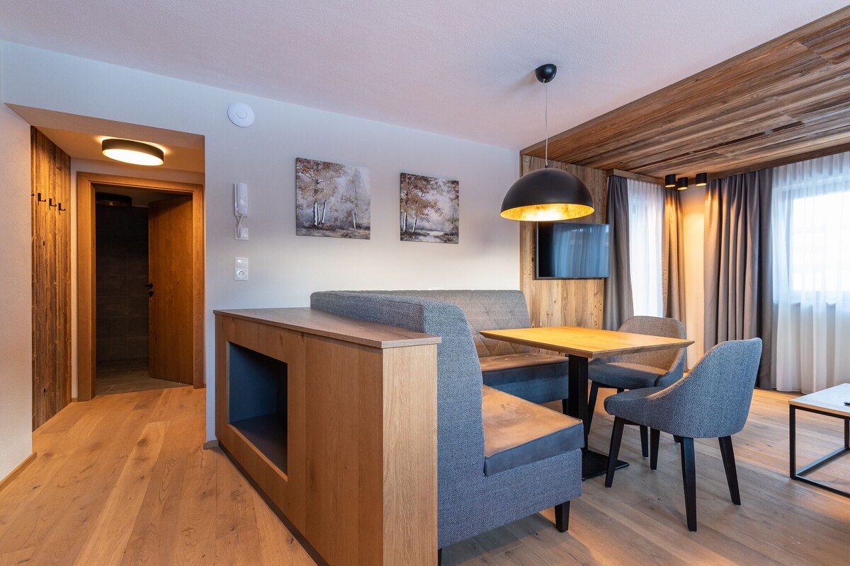 A modern living room with a wooden accent wall, a sofa, a dining table, and two chairs.